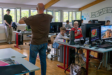 Lehrer erklärt Kindern in einem Computerraum in Österreich eine Lektion.